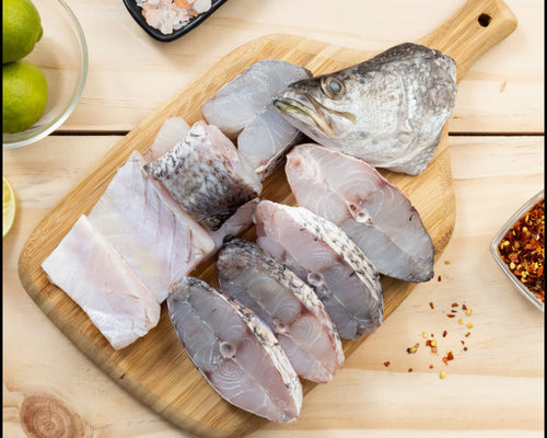 Raw fish fillets on a wooden cutting board with spices and limes on a wooden surface.