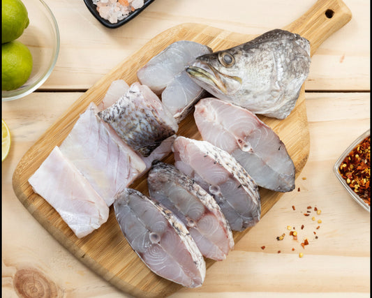 Raw fish fillets on a wooden cutting board with spices and limes on a wooden surface.